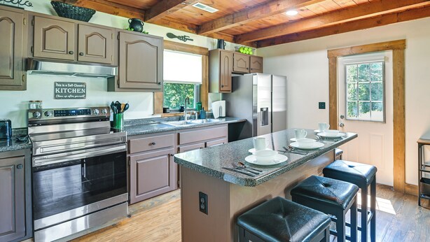 A kitchen with a stainless steel stove, a sink, and a large island with bar stools. - Creek, Trails & Falls! Rural Red River Gorge Cabin (Campton)