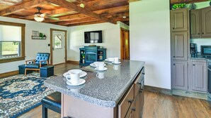 A kitchen with granite countertops, wooden cabinets, and a dining area with a blue rug and a blue chair. - Creek, Trails & Falls! Rural Red River Gorge Cabin (Campton)