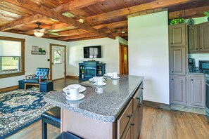 A kitchen with granite countertops, wooden cabinets, and a dining area with a blue rug and a blue chair.