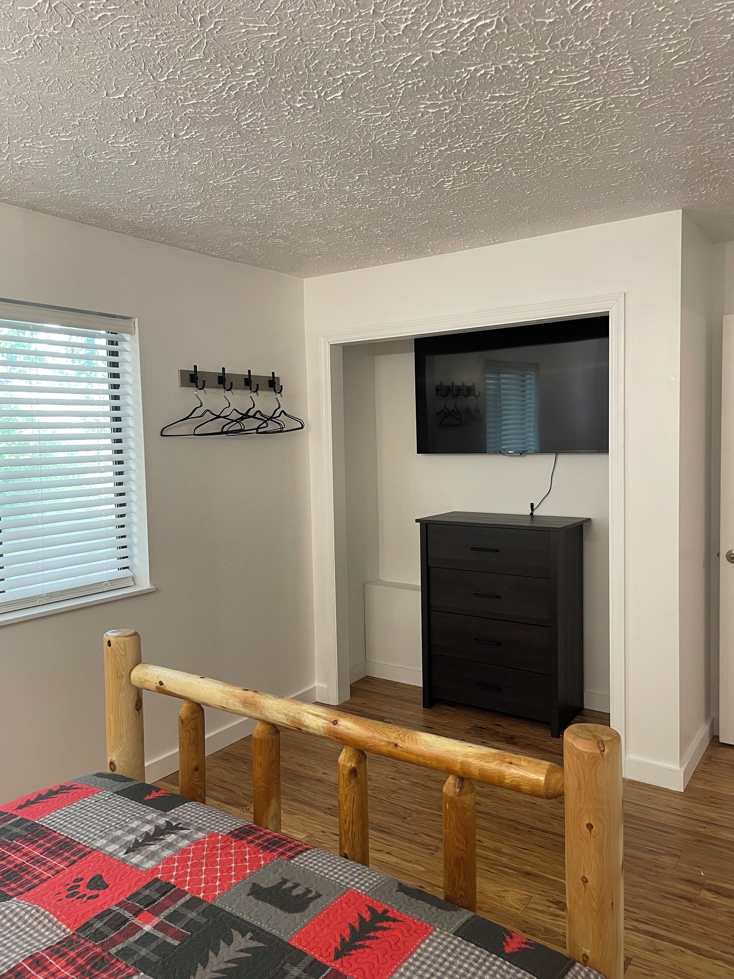 Una habitación con una escalera de madera, un aparador negro, un perchero y una ventana con persianas.