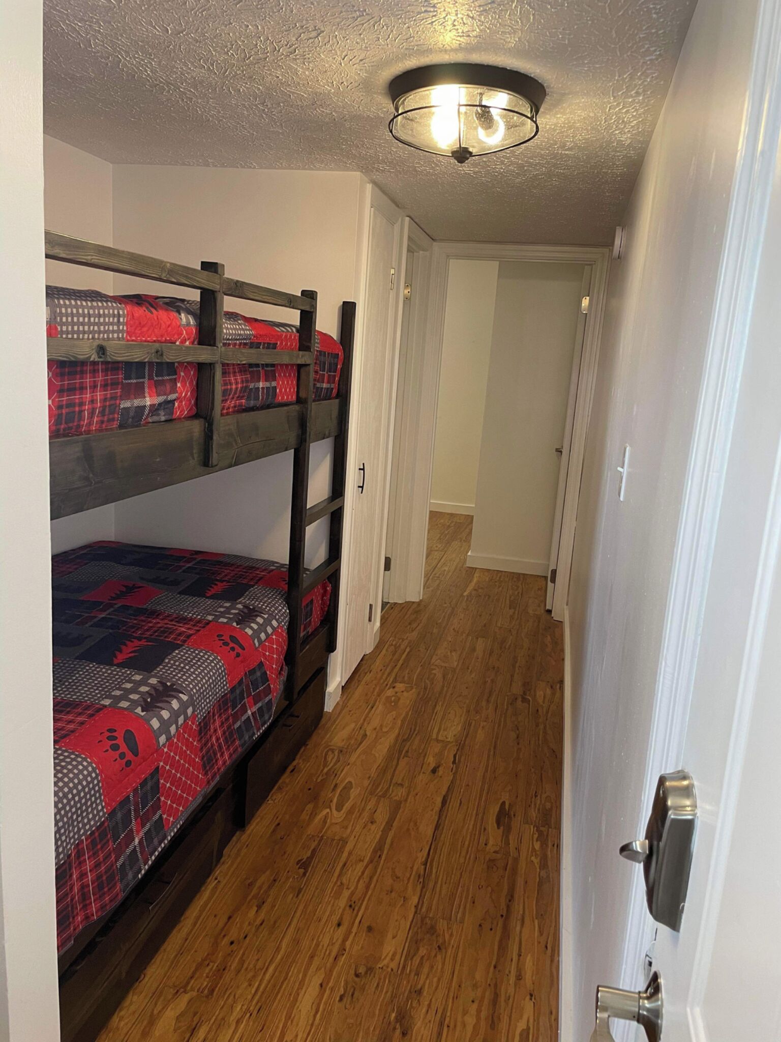 Una cama litera con ropa de cama roja y negra, suelo de madera y una puerta blanca.