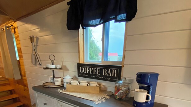 Un coin cuisine avec un panneau indiquant un bar à café, des meubles de rangement en bois et une fenêtre avec des rideaux.