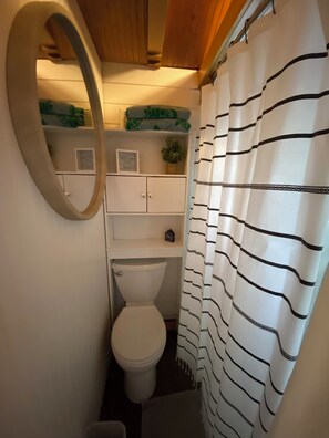 A compact bathroom with a toilet, a shelf with decorative items, and a striped shower curtain. - Tiny River Home Perfect Getaway (Decaturville)