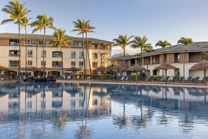 A hotel with a swimming pool, palm trees, and lounge chairs.