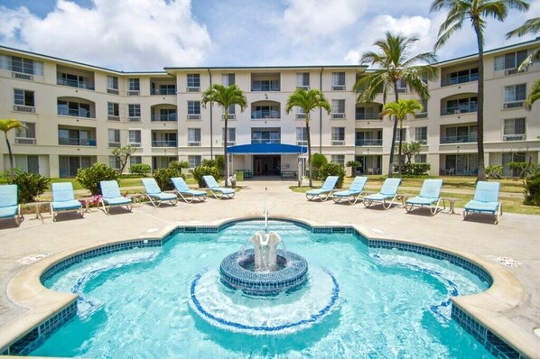 A hotel with a swimming pool, lounge chairs, and palm trees.
