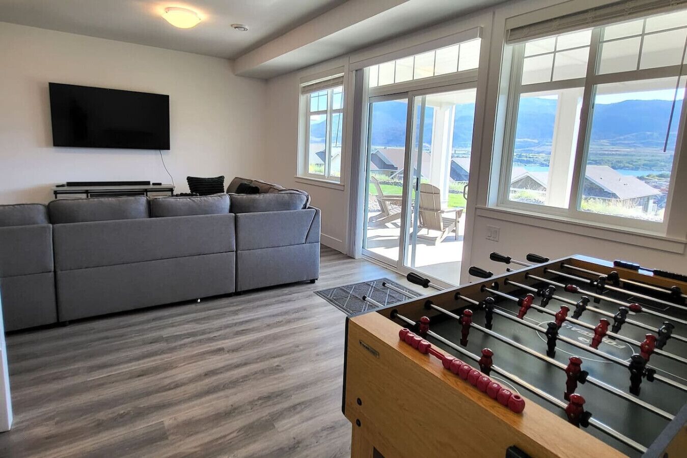 Ein Wohnzimmer mit grauem Sofa, einem Kicker und einem an der Wand befestigten Fernseher.