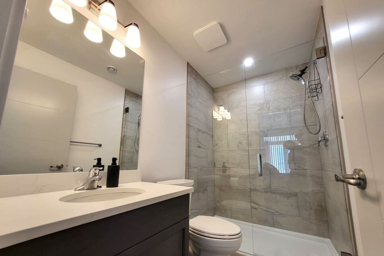 Un baño moderno con ducha de vidrio, tocador con espejo y un inodoro.