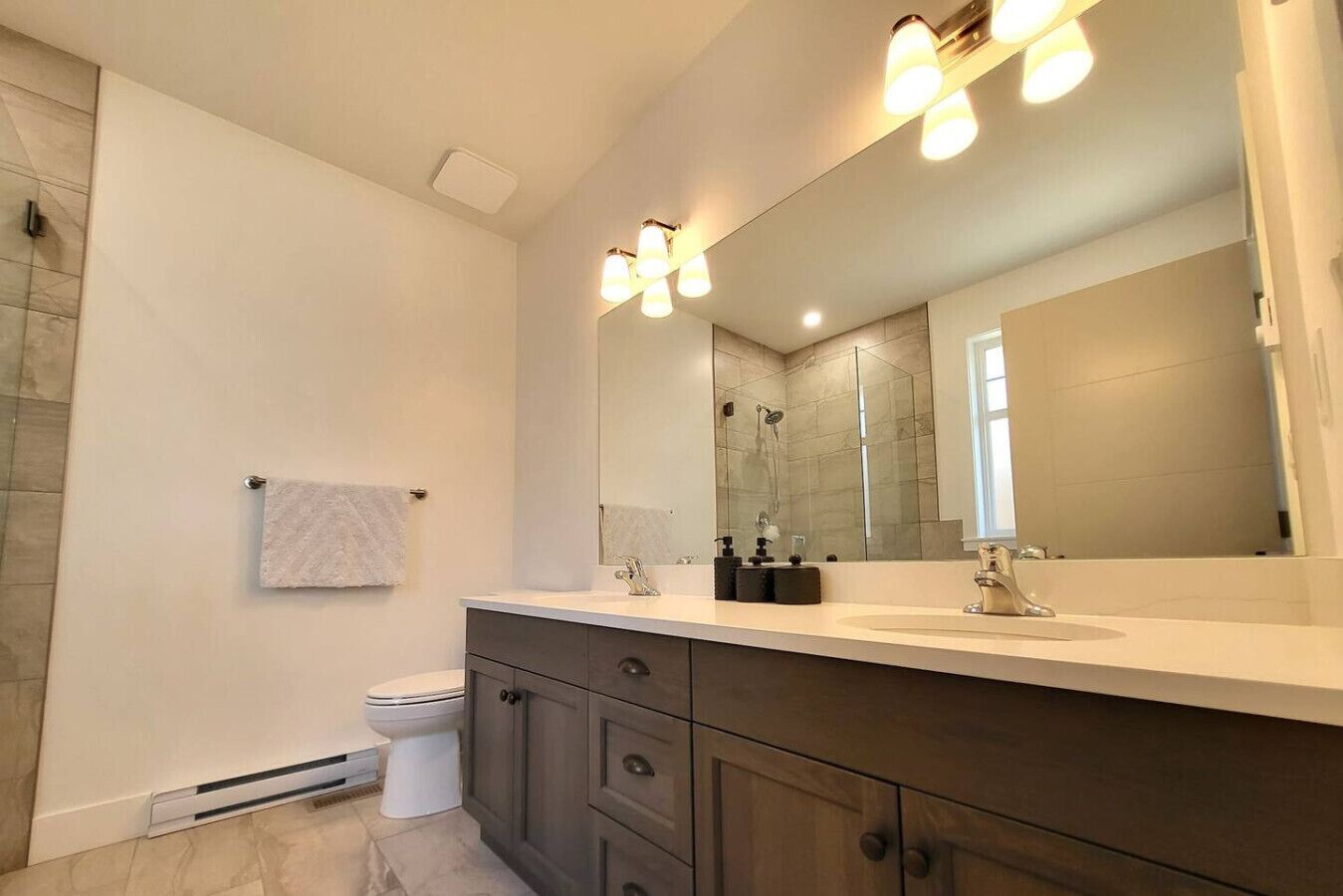 A modern bathroom with a large mirror, a toilet, and a vanity with a sink.