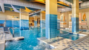 Ein Pool mit mehreren Wasserstrahlen, gefliesten Wänden und einer Poollandschaft mit Liege und Handtuchhalter.