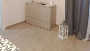 A bedroom with a bed, a dresser, a TV mounted on the wall, a small table with a lamp, and a window with curtains. - Rosetta's Experience (Roma)