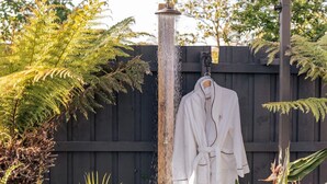 A white bathrobe hanging on a hook near a water feature in a garden setting. - Sol Coastal Retreat - Outdoor Spa and Sauna (Rosebud)