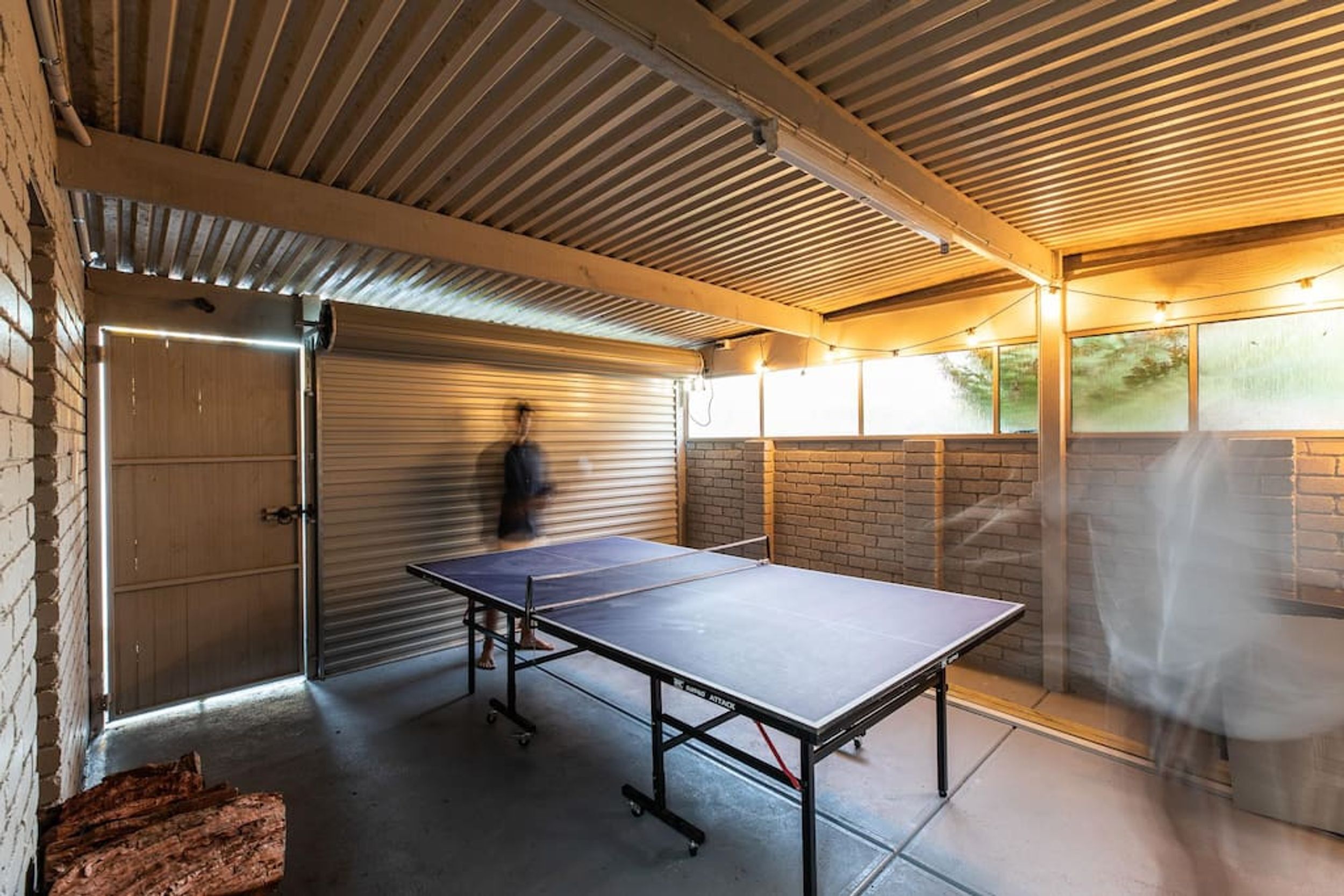 A ping pong table in a covered area with a brick wall and a sliding door.