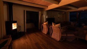 A cozy living room with a wood-burning stove, wicker chairs, and a sofa. - Sol Coastal Retreat - Outdoor Spa and Sauna (Rosebud)