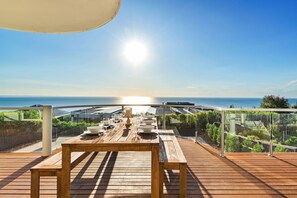 Une terrasse en bois avec une table dressée pour le repas, offrant une vue sur la côte.