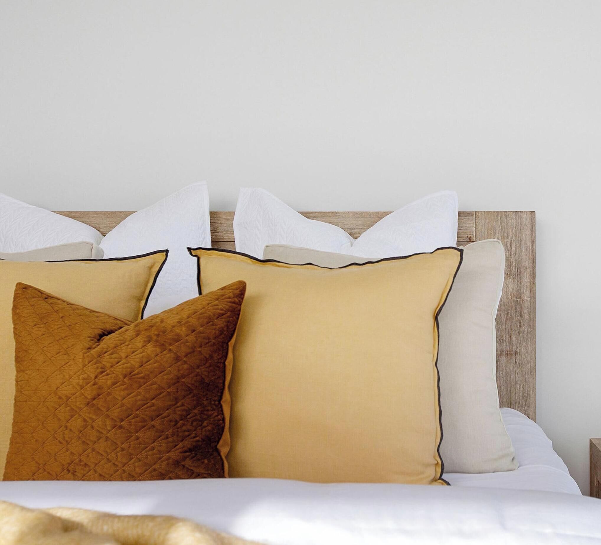 Un lit avec une tête de lit en bois, des oreillers blancs et bruns, et une couverture blanche.