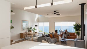 A spacious living area with a large window overlooking the sea, a dining area, and a cozy seating area with a fireplace. - Clifftop Luxury With Spectacular Ocean Views (Mount Martha)