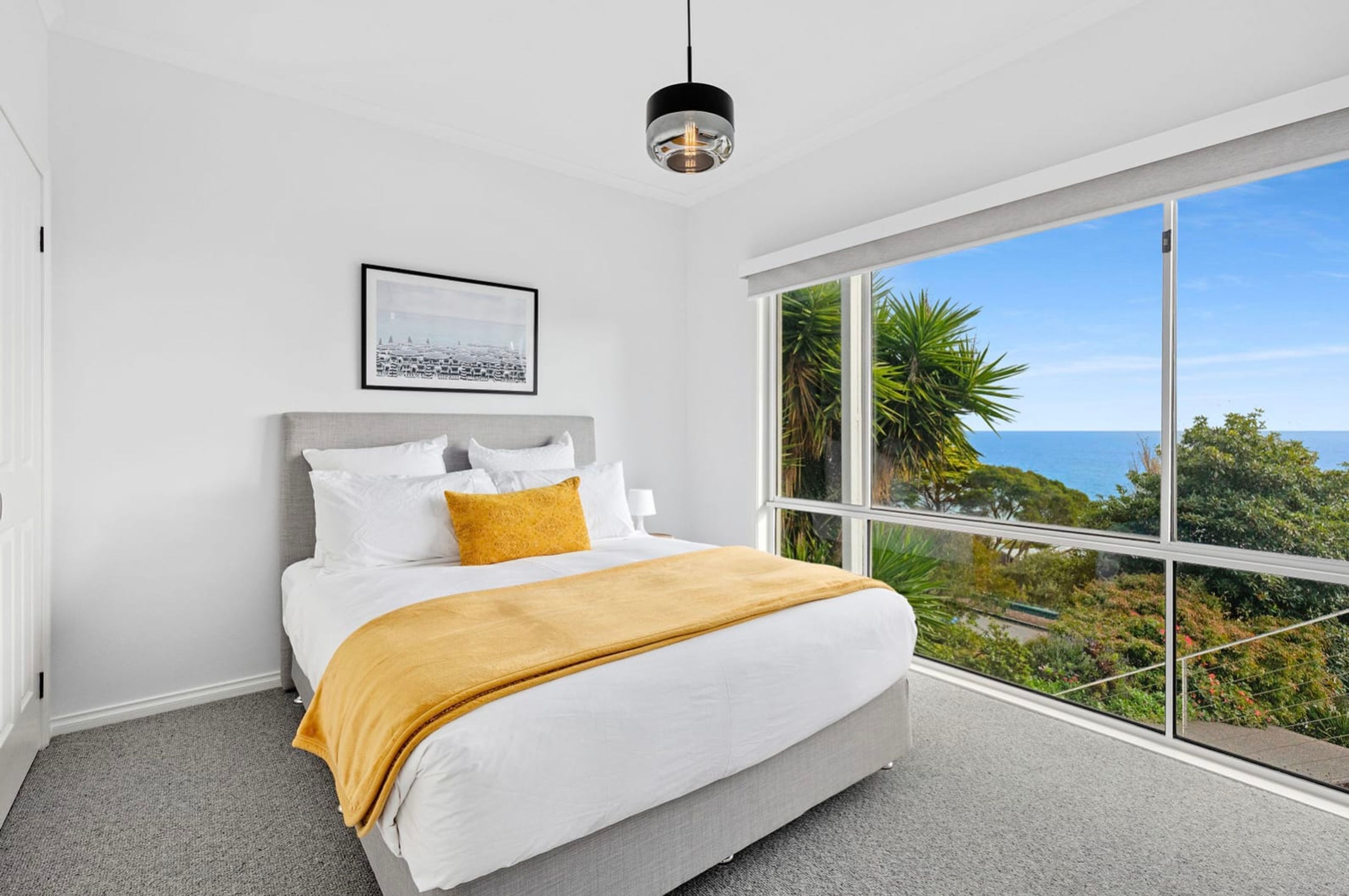 Un dormitorio con un amplio ventanal que ofrece vistas al mar y a la vegetación.