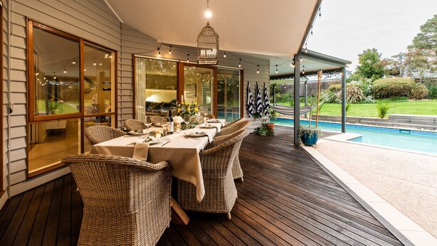 An outdoor dining area with wicker furniture, a pool, and a covered section with a hanging light fixture. - Hamptons Inspired Luxury (Mount Martha)