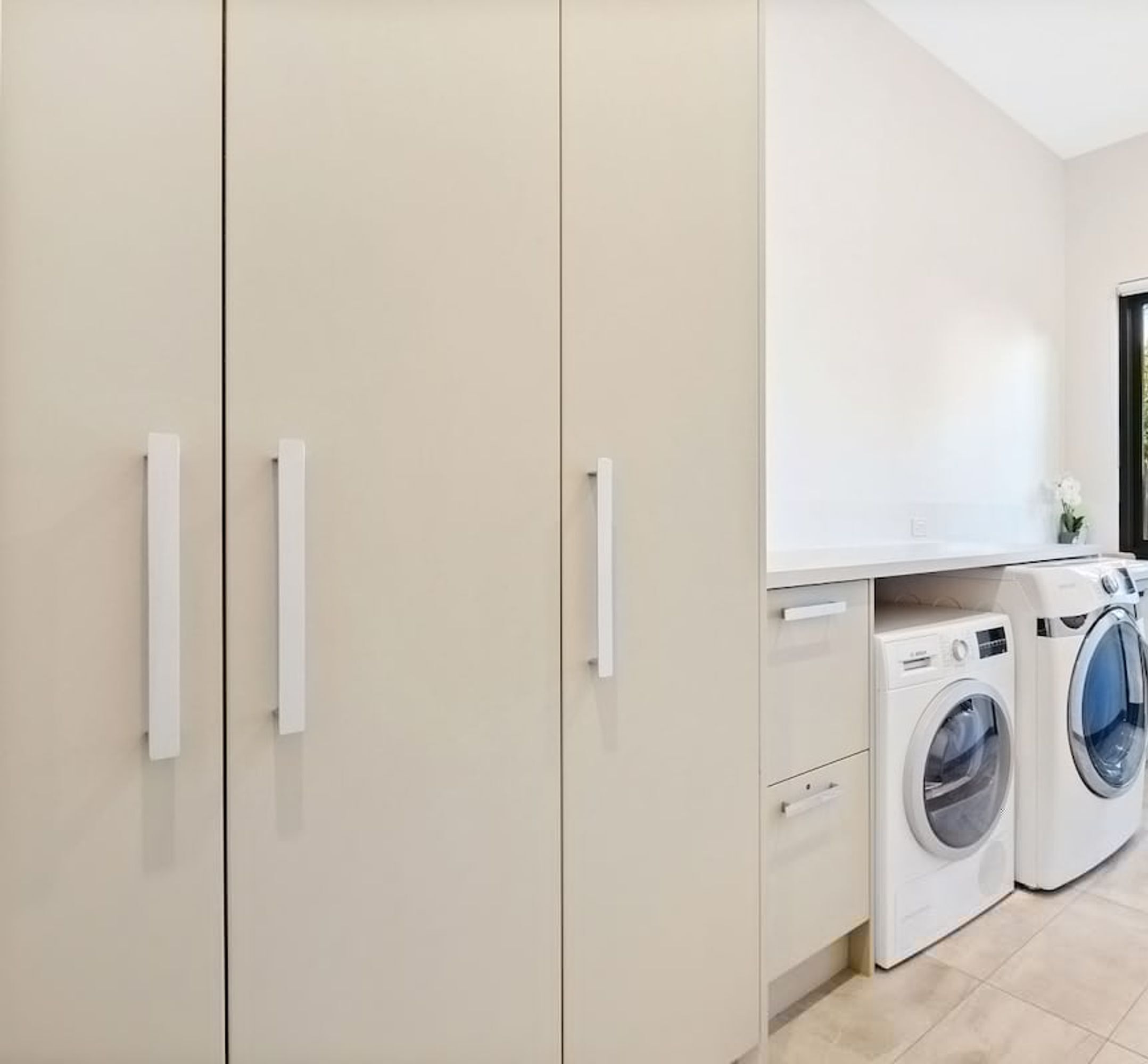 A laundry room with two washing machines, beige cabinets, and a white countertop.