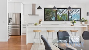 A modern kitchen with white cabinetry, stainless steel appliances, and a large window offering a view of trees.