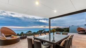 A modern outdoor patio with a glass table and wicker furniture, overlooking a scenic ocean view.
