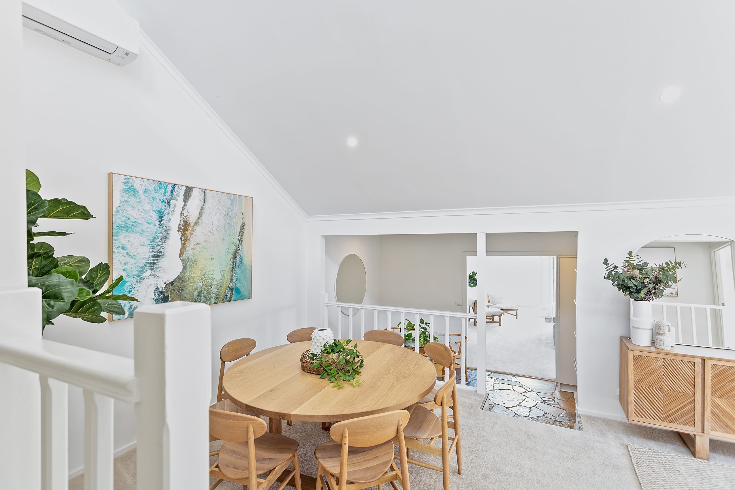 Et moderne spiseområde med et rundt træbord, seks stole og et hvidt loft.