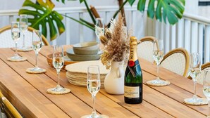 Une table de salle à manger en bois, mise avec des verres à vin, une bouteille de champagne et un vase décoratif contenant des fleurs séchées.