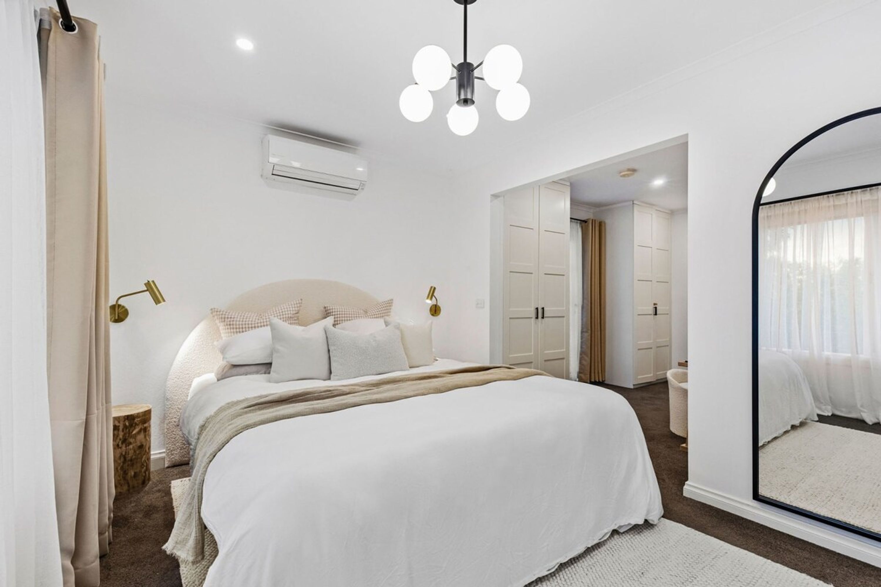 A bedroom with a large bed, a ceiling light, an air conditioning unit, and a mirror.