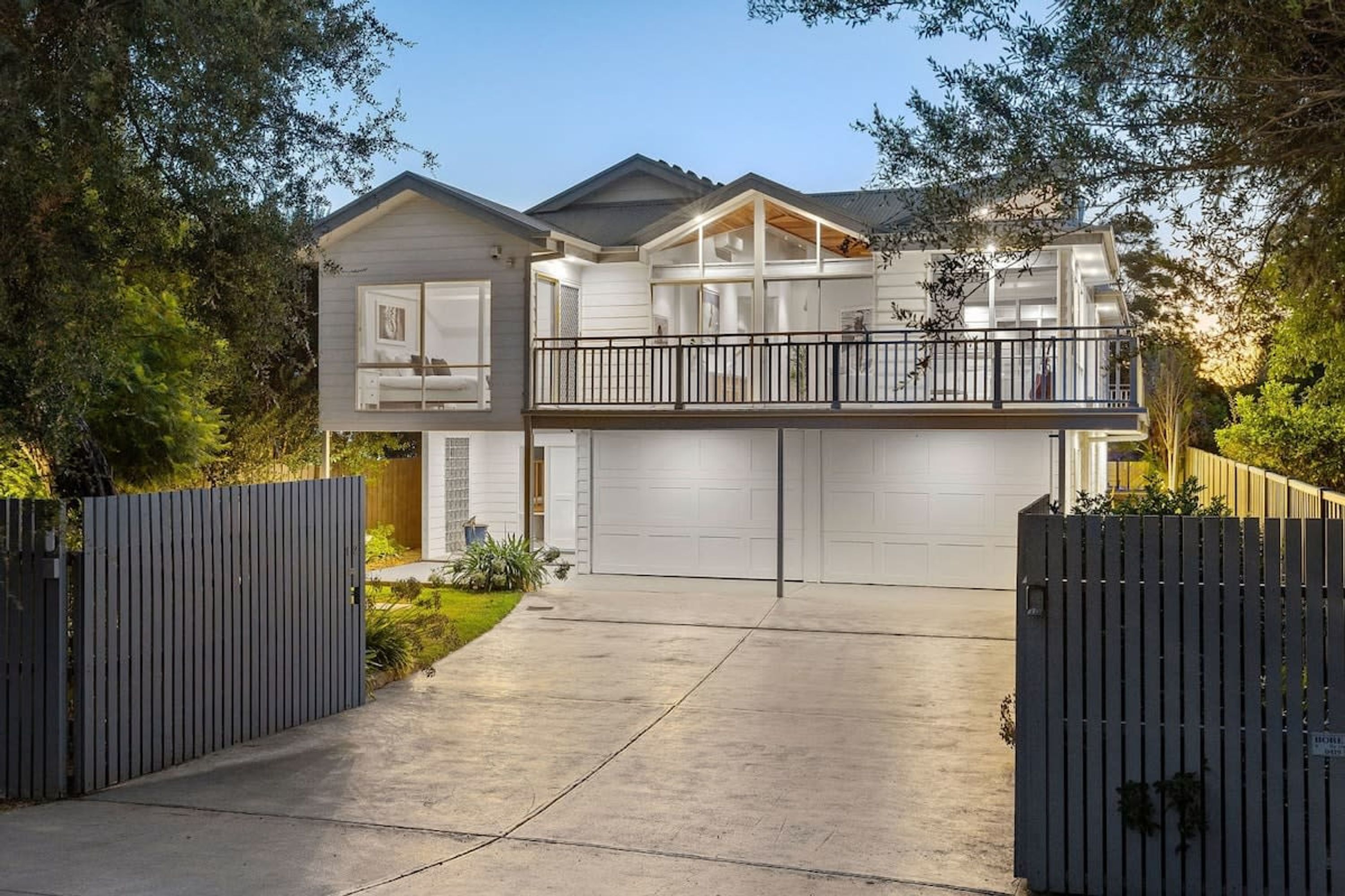 A two-story house with a balcony, a garage, and a fenced driveway.
