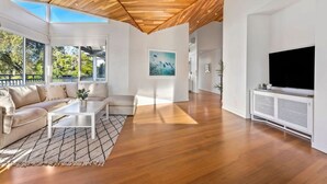 A spacious living room with a wooden ceiling, large windows, a white sofa, a coffee table, and a TV on a white console. - Blairgowrie Beachside Retreat Solar Heated Pool (Blairgowrie)