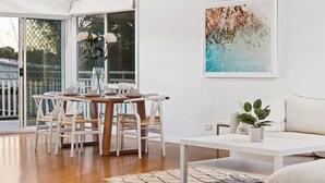 A modern dining area with a wooden table and white chairs, a white sofa, and a large abstract painting on the wall. - Blairgowrie Beachside Retreat Solar Heated Pool (Blairgowrie)