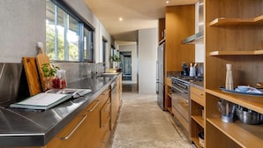 A modern kitchen with stainless steel appliances, wooden cabinetry, and a view through the window. - Luxury Portsea Sanctuary Gas Heat Pool Gardens (Portsea)