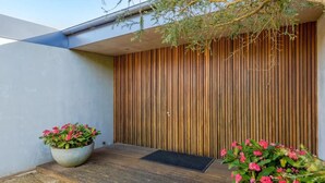 A modern building with a wooden slatted wall, a concrete floor, and two potted plants with pink flowers. - Luxury Portsea Sanctuary Gas Heat Pool Gardens (Portsea)