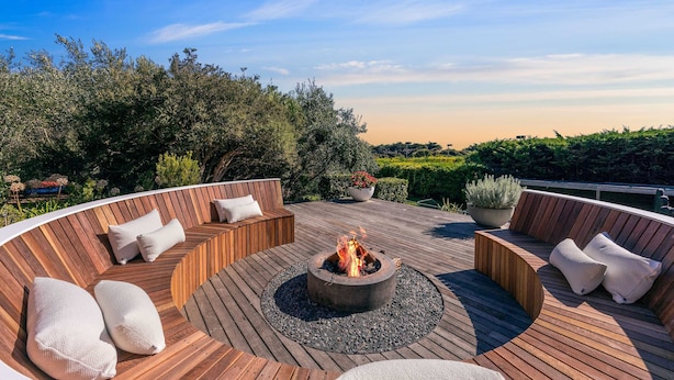 A circular wooden deck with a fire pit, seating, and potted plants. - Luxury Portsea Sanctuary Gas Heat Pool Gardens (Portsea)