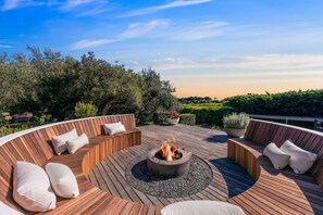 Eine runde Holzterrasse mit Feuerstelle, Sitzgelegenheiten und Blumentöpfen.