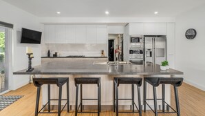 A modern kitchen with white cabinets, a large island with bar stools, a built-in oven, and a microwave. - Modern Waterfront Retreat Private Pool Dock (Gold Coast)