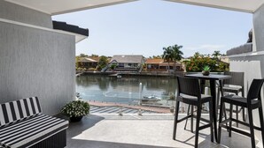 A covered outdoor area with a seating arrangement, a table, and a view of a body of water and buildings in the background. - Modern Waterfront Retreat Private Pool Dock (Gold Coast)