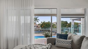 A modern living room with a sofa, a blanket, and a view of a pool and outdoor area. - Modern Waterfront Retreat Private Pool Dock (Gold Coast)