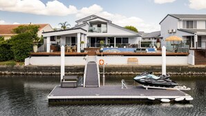 A modern house with a dock, a jet ski, and a lifebuoy. - Modern Waterfront Retreat Private Pool Dock (Gold Coast)