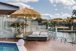 Eine Terrasse mit einer Rattan-Couch, einem Reedschirm und einem Blumentopf.
