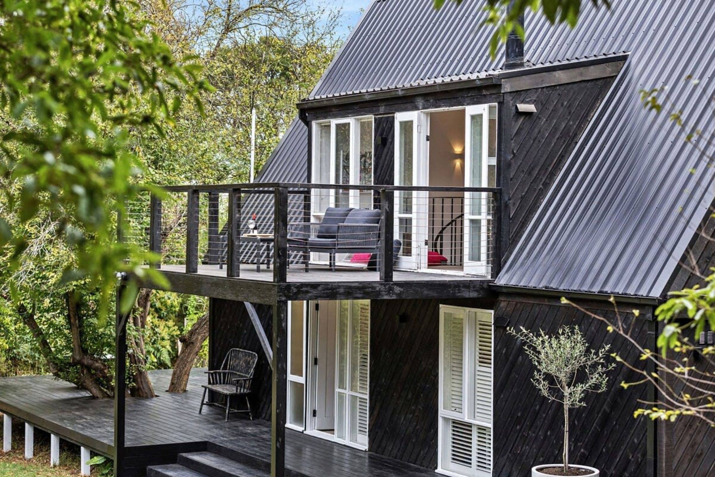 A modern two-story house with a balcony, a wooden deck, and a small garden area.