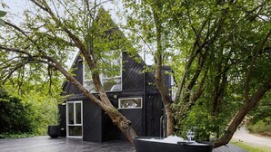 A modern house with a black exterior, surrounded by lush greenery and a wooden deck. - The Coast Country Cottage (Balnarring Beach)