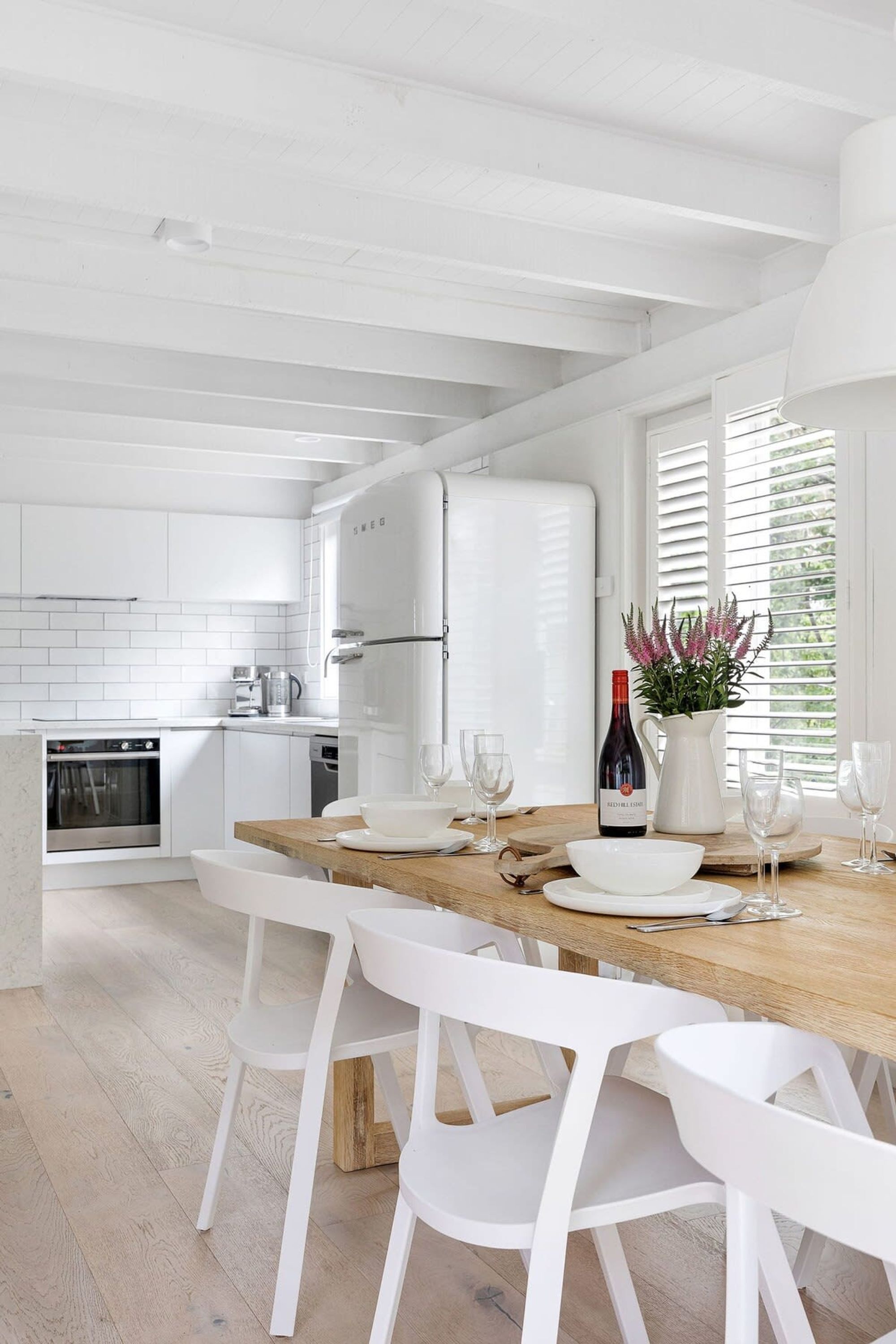 Une cuisine moderne avec des meubles blancs, une table à manger en bois et des chaises blanches.