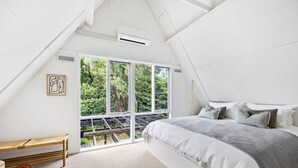 A bedroom with a large bed, a bench, and a window with a view of greenery. - The Coast Country Cottage (Balnarring Beach)