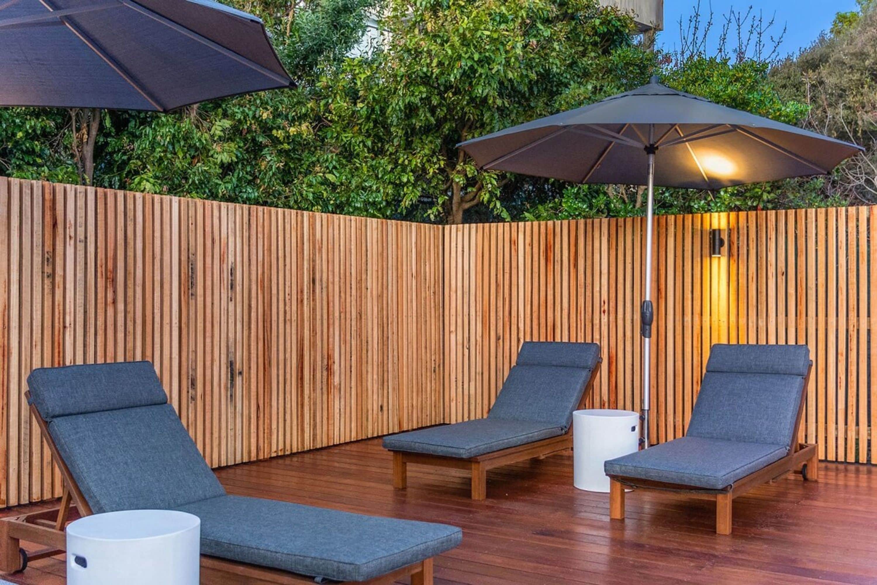 Una terraza de madera con tres sillas de descanso y dos sombrillas.