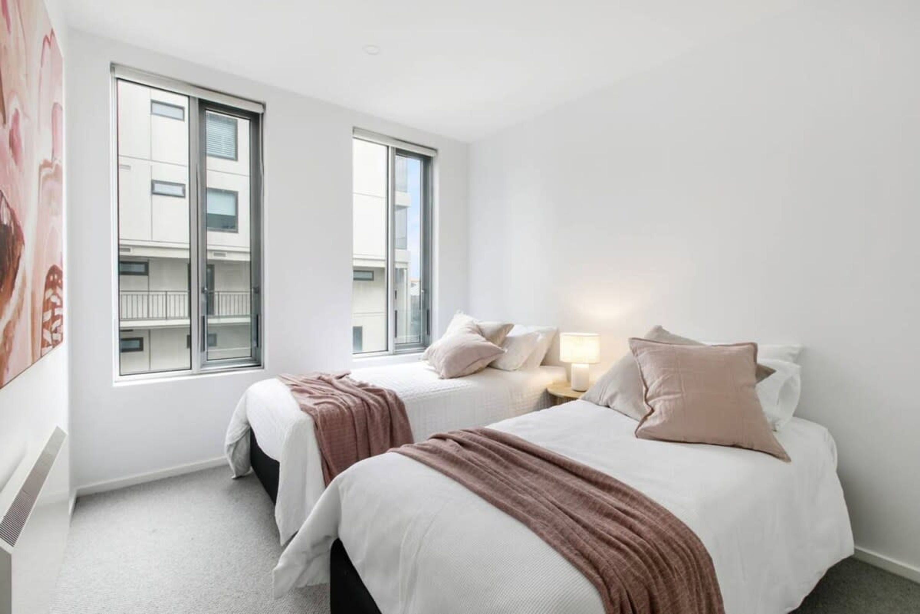 A hotel room with two beds, a large window, and a view of the building outside.