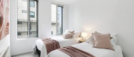 A hotel room with two beds, a large window, and a view of the building outside.