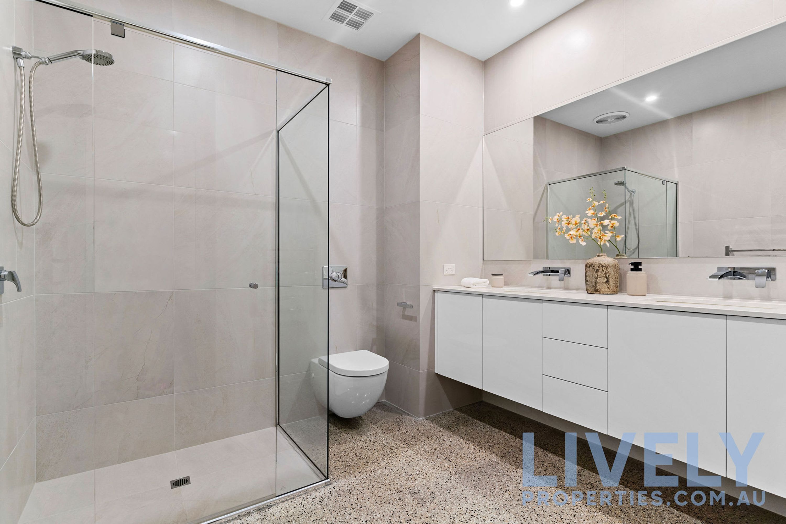 A modern bathroom with a glass-enclosed shower, a toilet, and a vanity with a mirror.