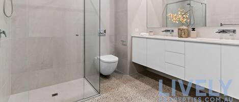 A modern bathroom with a glass-enclosed shower, a toilet, and a vanity with a mirror.