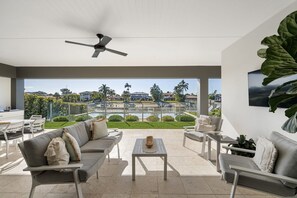 A modern outdoor living area with a sofa, chairs, a table, and a ceiling fan. - Luxe Family Entertainer on Canal Private Pool (Gold Coast)